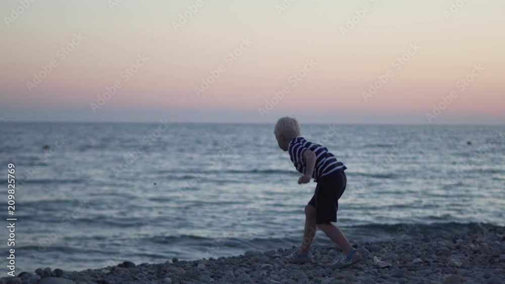 the boy in a striped T-shirt throws stones at the sea at sunset. the boy in a striped T-shirt throws stones at the sea at sunset.