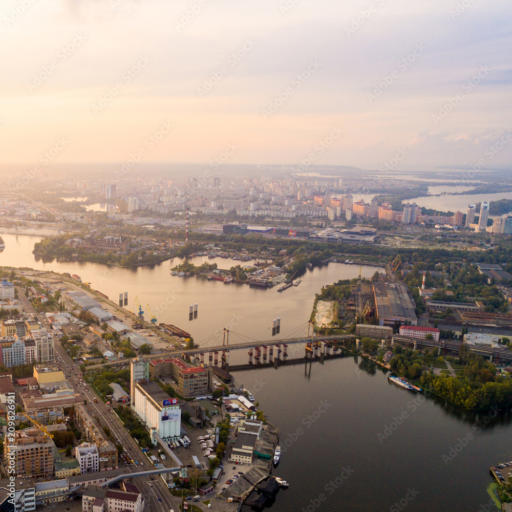 Panoramic view of a modern city with a river. Skyline bird eye aerial view of the old part of the city - Podol district under dramatic cloud sunset sky. Rybalsky Island. Kiev. Ukraine