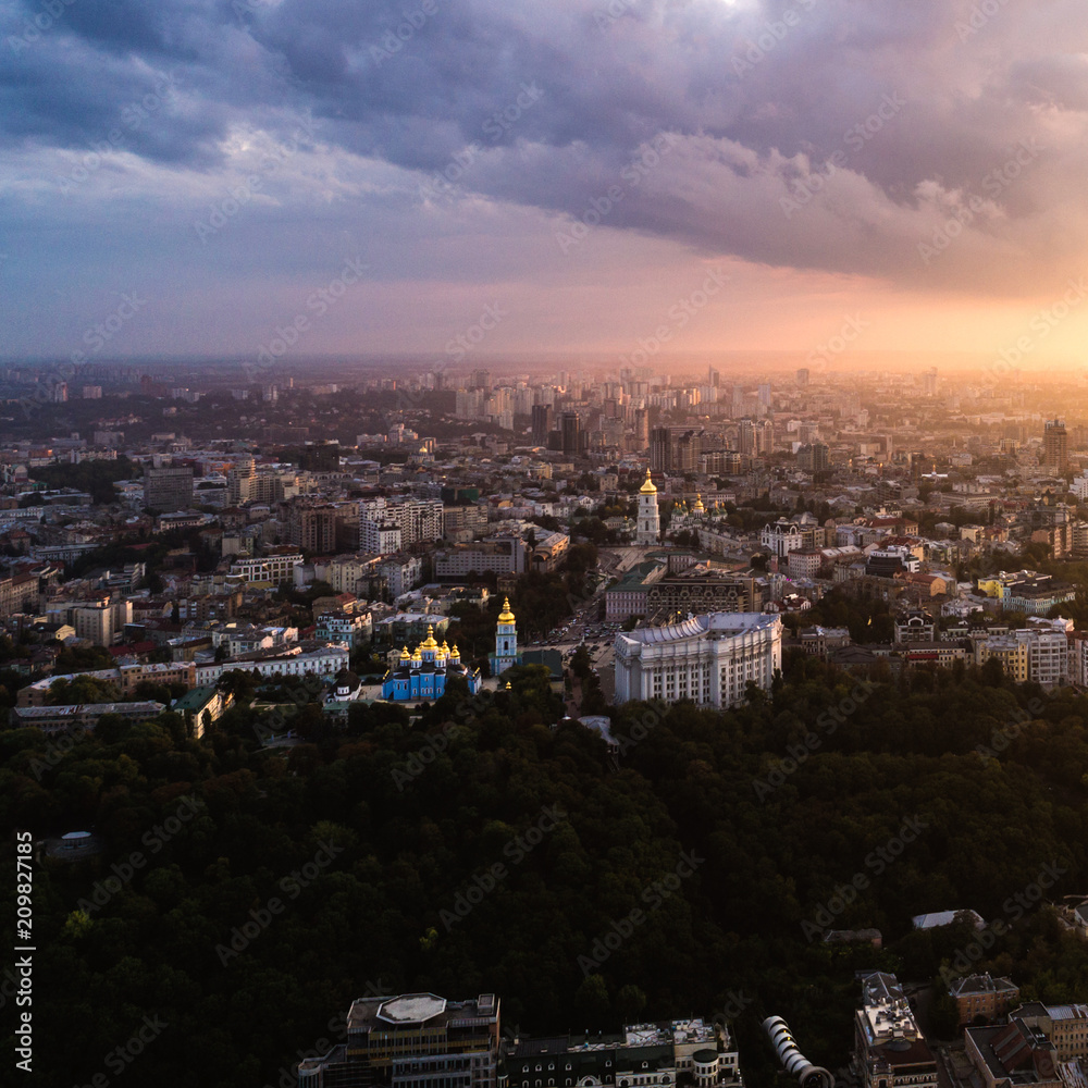 Panoramic view of a modern city at sunset. Skyline bird eye aerial view of the old part of the city under dramatic cloud sunset sky. Vladimirskaya Gorka, St. Andrew's Church, St. Michael's Golden