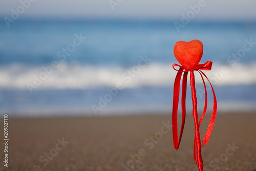 Valentine's day greeting card concept, red heart on pristine sandy beach, honeymoon vacation background. photo