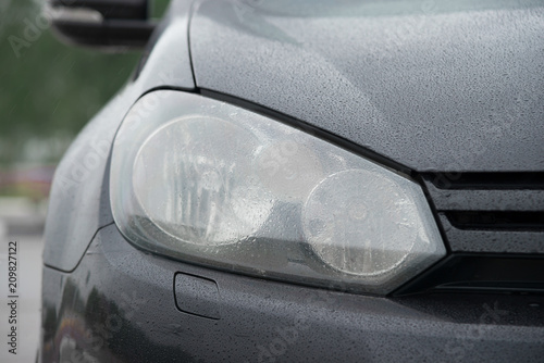Black sports car front light with dew after the rain coseup