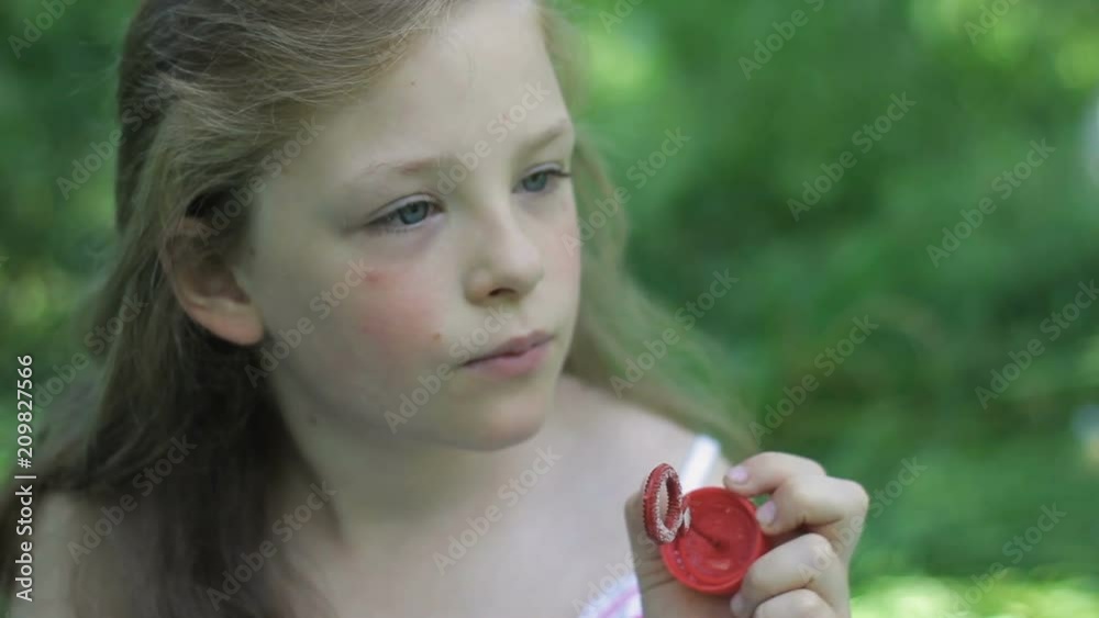 Cute lovely little girl sitting on green grass blowing soap bubbles and relaxing Cute lovely little girl sitting on green grass blowing soap bubbles and relaxing