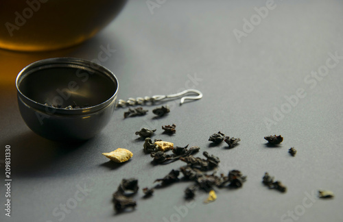 Tea strainer with a glass cup and scattered tea on grey background
