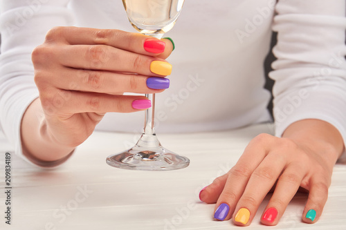 Manicured hands holding glass of champagne. Female summer manicure and champagne glass. Perfect multicolored manicure.