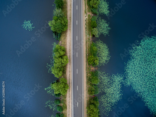 Landscape of an asphalt road. View from above on the road going along the blue river. Summer photography with bird's eye view