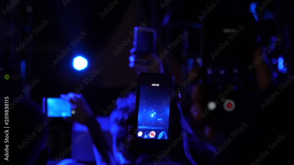 Fan spectators stay by concert stage hold mobile phones shooting video of music performance in night lights lumiere