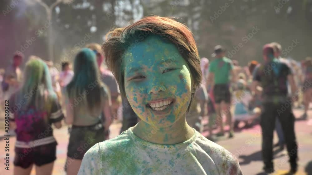 Young happy asian girl is smiling with colourful powder on holi festival in daytime in summer, watching at camera, color concept