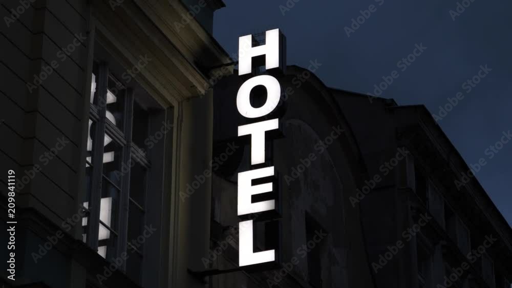 Hotel neon vertical signboard on a building wall shining at night street in Europe Hotel neon vertical signboard on a building wall shining at night street in Europe