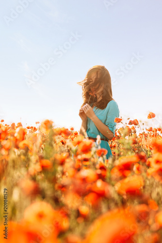 Young woman sniffing a poppy in meadow.