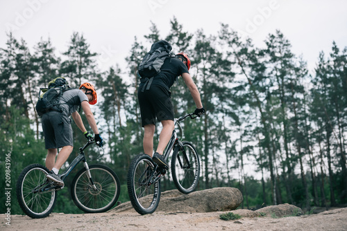 two male extreme cyclists in protective helmets riding on mountain bicycles in forest