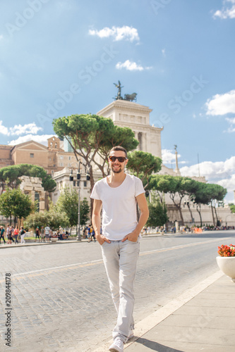 Photography young male tourist in white clothes and sunglasses walking in the center of Rome