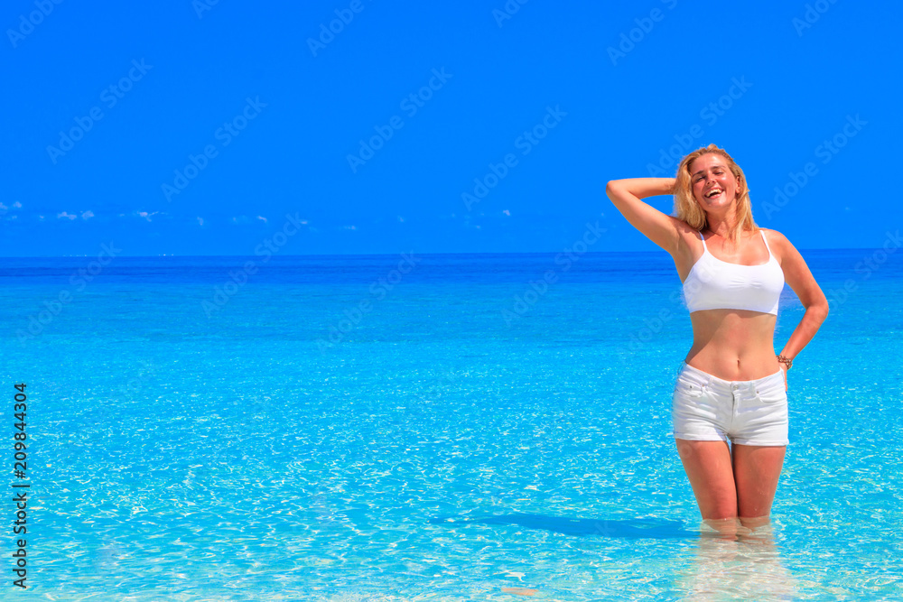 Gorgeous blond woman with white clothes is standing in the water at the sandy beach Gorgeous blond woman with white clothes is standing in the water at the sandy beach