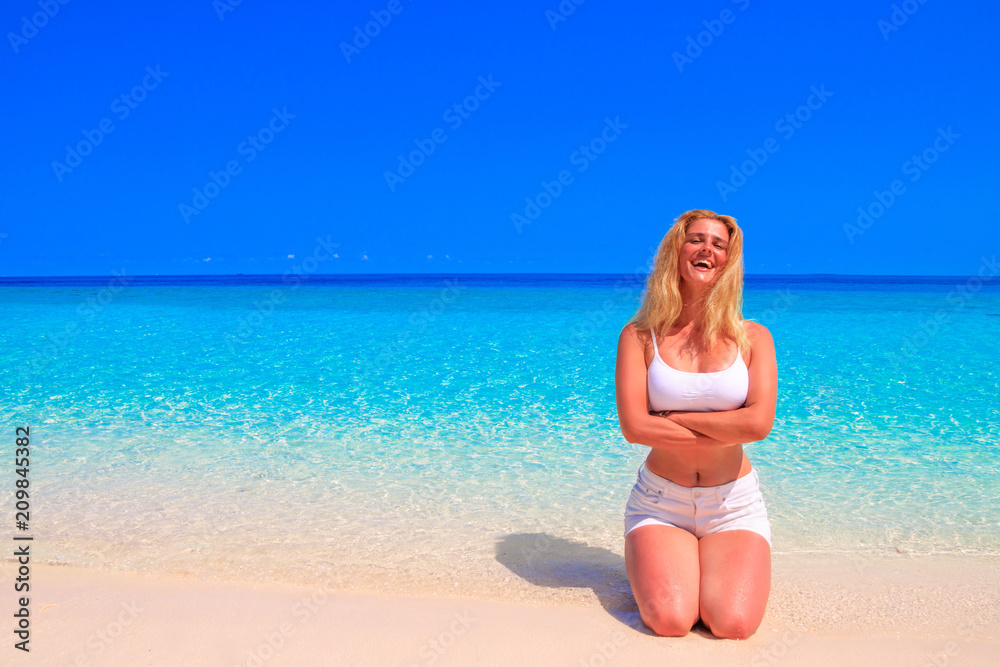 Gorgeous blond woman in white clothes is kneeling on the sandy beach Gorgeous blond woman in white clothes is kneeling on the sandy beach