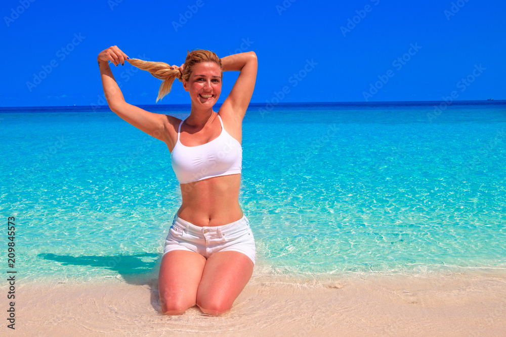 Gorgeous blond woman in white clothes is kneeling on the sandy beach Gorgeous blond woman in white clothes is kneeling on the sandy beach