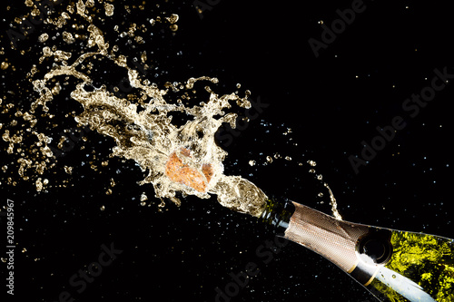 Celebration of birthday, anniversary or Christmas theme. Explosion of splashing champagne sparkling wine with flying cork out of the bottle on black background. photo