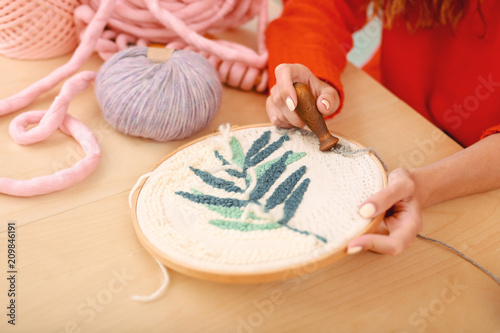 Floral picture. Skillful red-haired housewife wearing knitted red sweater embroidering little beautiful floral picture