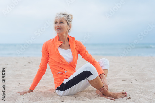 Fototapeta Naklejka Na Ścianę i Meble -  ältere frau sitz am strand und dehnt sich nach dem sport