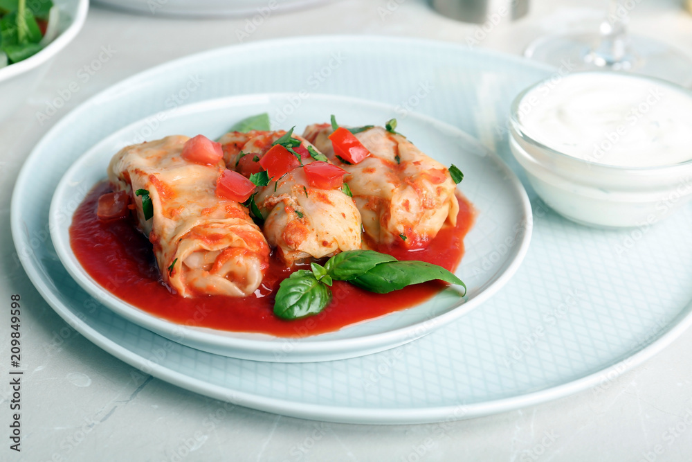 Plate with stuffed cabbage leaves in tomato sauce on table