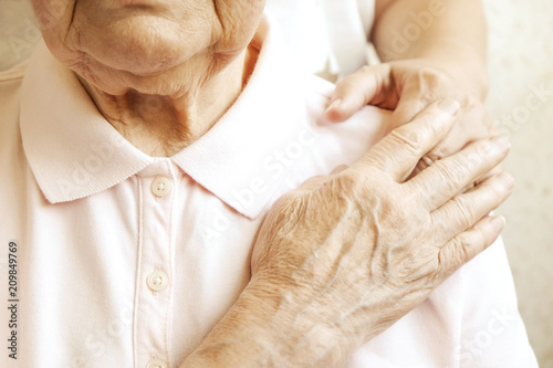 Mature female in elderly care facility gets help from hospital personnel nurse. Senior woman, aged wrinkled skin & hands of her care giver. Grand mother everyday life. Background, copy space, close up