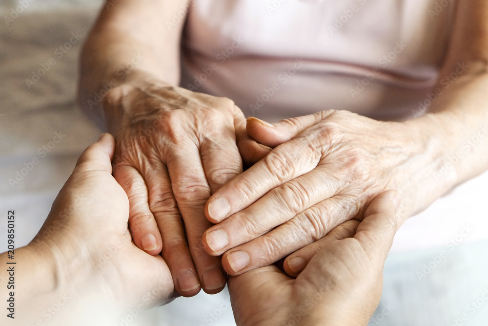Fototapeta premium Mature female in elderly care facility gets help from hospital personnel nurse. Senior woman w/ aged wrinkled skin & care giver, hands close up. Grand mother everyday life. Background, copy space.