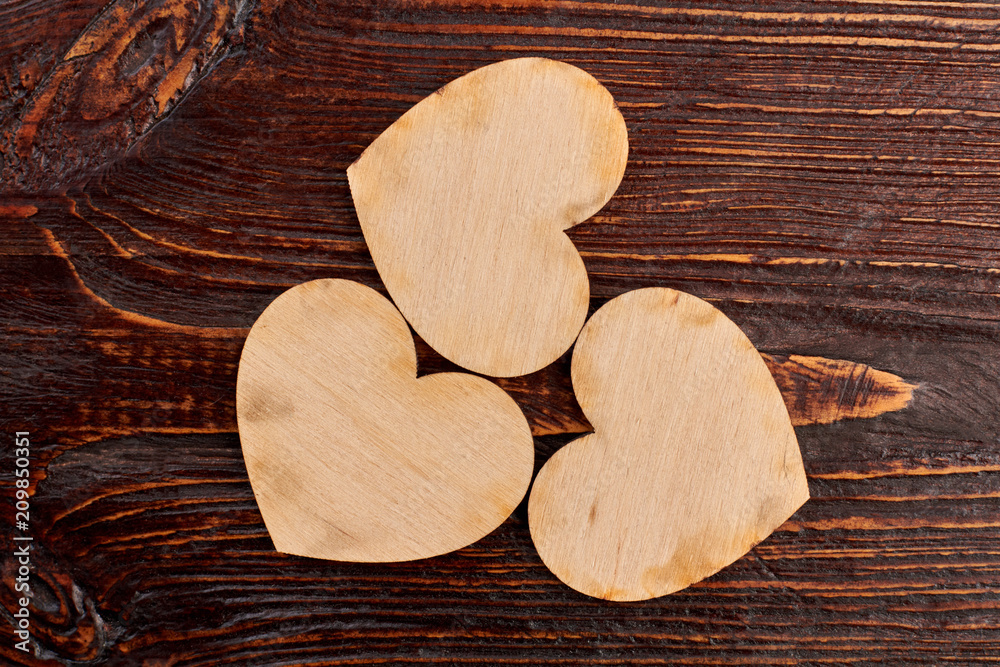 Obraz premium Three wooden hearts, top view. Vintage style wooden hearts on dark wooden background. Valentines holiday greeting card.