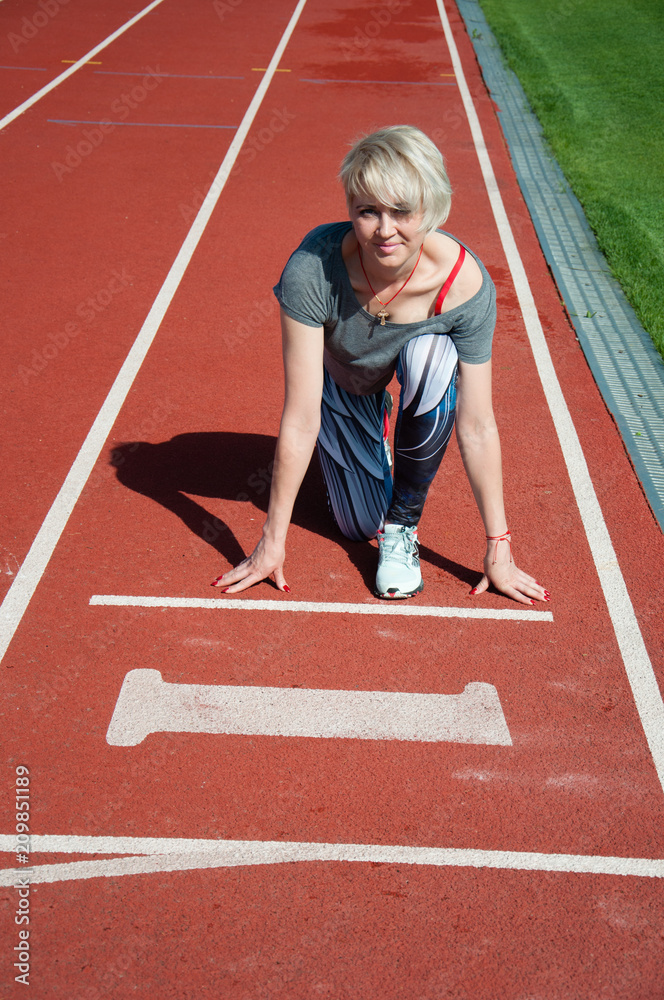 Obraz premium Sports woman fitness athlete at the start near the stadium, preparing for the sprint. Fitness, the concept of a healthy lifestyle