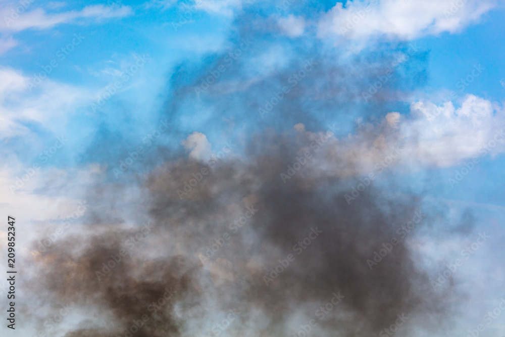 Black smoke against a blue sky with clouds