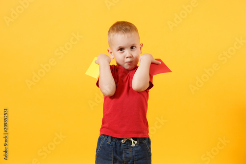 Little cute kid baby boy in red t-shirt holding in hand yellow and red soccer referee cards for retire from field isolated on yellow background. Kids sport family leisure lifestyle concept. Copy space