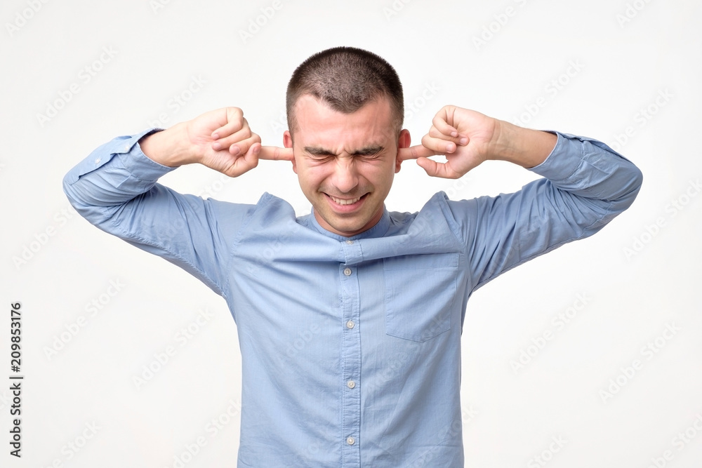 Stressed frustrated young man plugging his ears and keeping eyes closed. Stressed frustrated young man plugging his ears and keeping eyes closed.