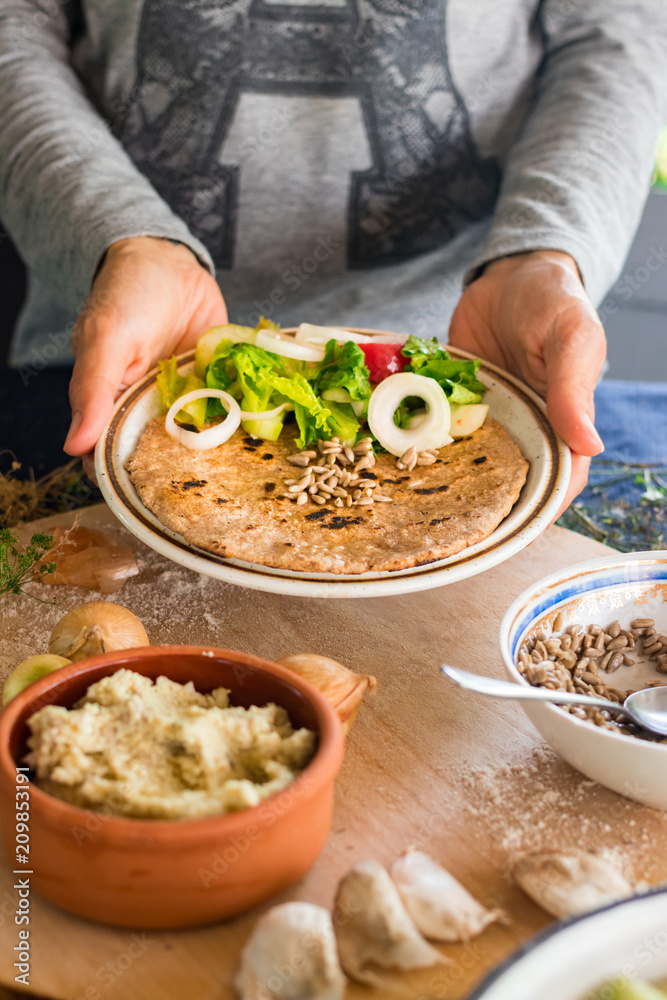 Woman hands holds garlic naan bread with butter, seeds and vegetables salad. Traditional Indian asian plain flatbread made with whole wheat flour. Raw vegan vegetarian healthy food