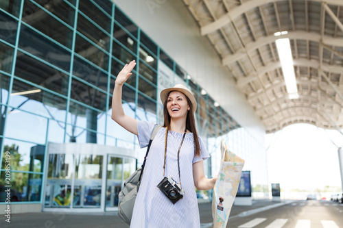 Obraz na płótnie Traveler tourist woman with retro vintage photo camera, paper map waving hand for greeting, meeting friend and catch taxi at airport