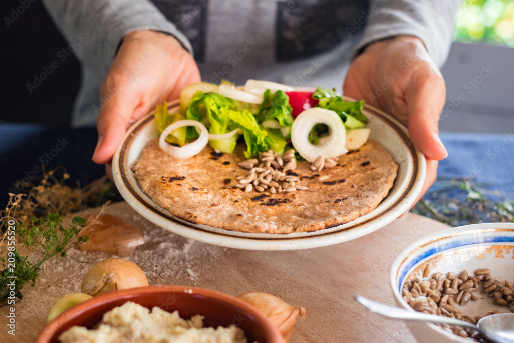 Woman hands holds garlic naan bread with butter, seeds and vegetables salad. Traditional Indian asian plain flatbread made with whole wheat flour. Raw vegan vegetarian healthy food