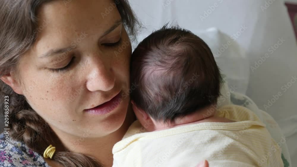 A tired mother burping a newborn girl after nursing her in the hospital A tired mother burping a newborn girl after nursing her in the hospital
