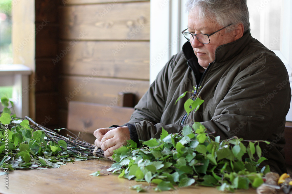 Fototapeta premium Senior man preparing birch broom for the bath. Traditional nothern spa attribute.