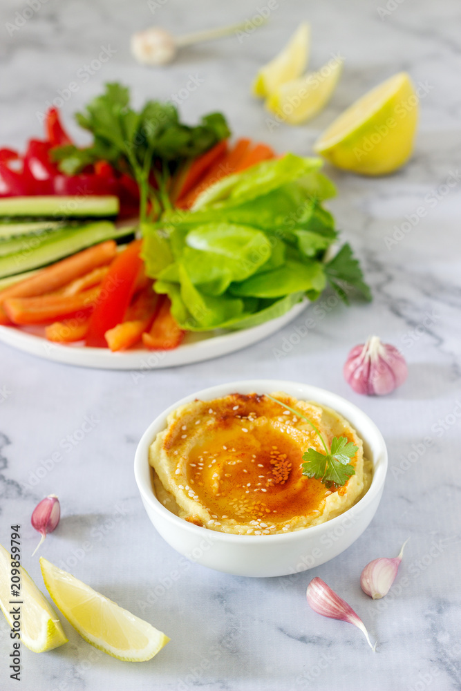 Hummus, different vegetables and lettuce leaves with lemon and garlic on a light background. Vegan food. Hummus, different vegetables and lettuce leaves with lemon and garlic on a light background. Vegan food.