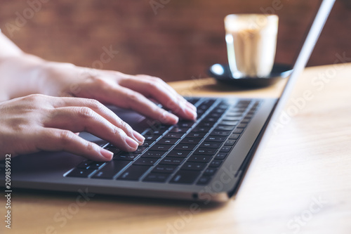 Closeup image of hands working and typing on laptop keyboard with coffee cup on wooden table