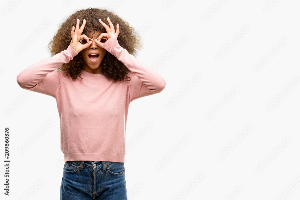 African american woman wearing pink sunglasses doing ok gesture like binoculars sticking tongue out, eyes looking through fingers. Crazy expression. African american woman wearing pink sunglasses doing ok gesture like binoculars sticking tongue out, eyes looking through fingers. Crazy expression.