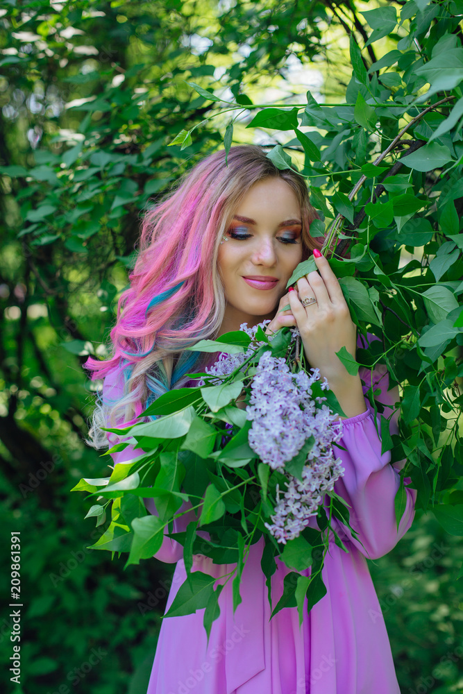 Beautiful girl with colorful dyed hair and perfect makeup and hairstyle standig next to lilac bush