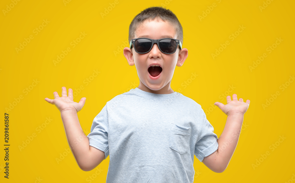 Dark haired little child wearing sunglasses very happy and excited, winner expression celebrating victory screaming with big smile and raised hands Dark haired little child wearing sunglasses very happy and excited, winner expression celebrating victory screaming with big smile and raised hands