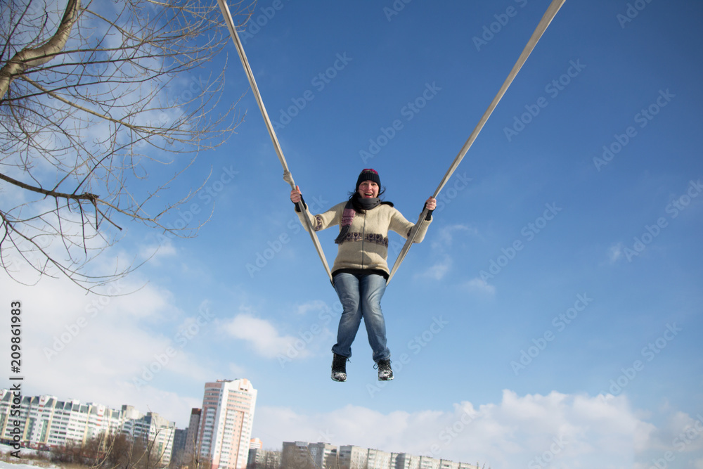 An adult woman rides high on a rope swing