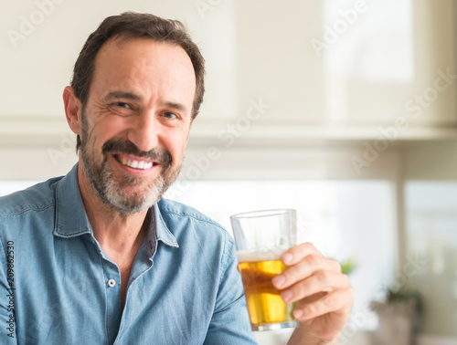 Middle age man drinking beer with a happy face standing and smiling with a confident smile showing teeth