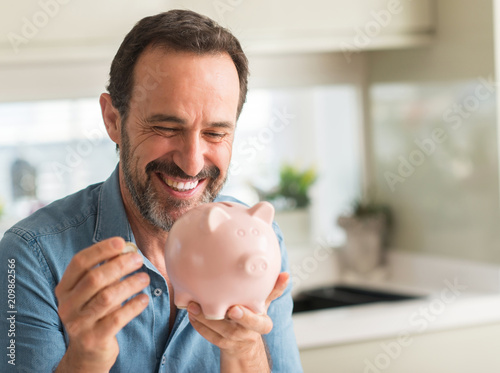 Middle age man save money on piggy bank with a happy face standing and smiling with a confident smile showing teeth photo
