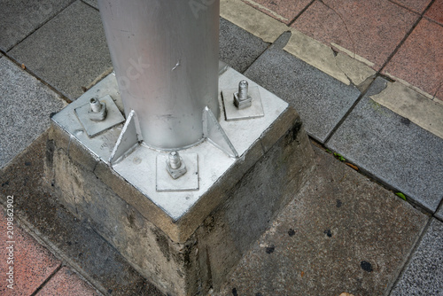 Metal pole with screw on concrete foundation in public space area.