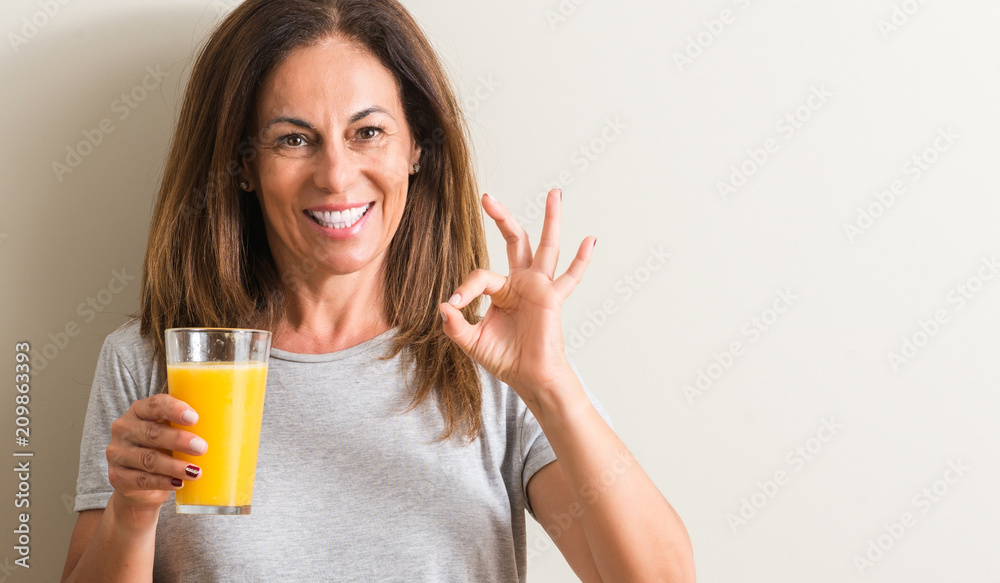 Middle age woman drinking orange juice in a glass doing ok sign with fingers, excellent symbol Middle age woman drinking orange juice in a glass doing ok sign with fingers, excellent symbol