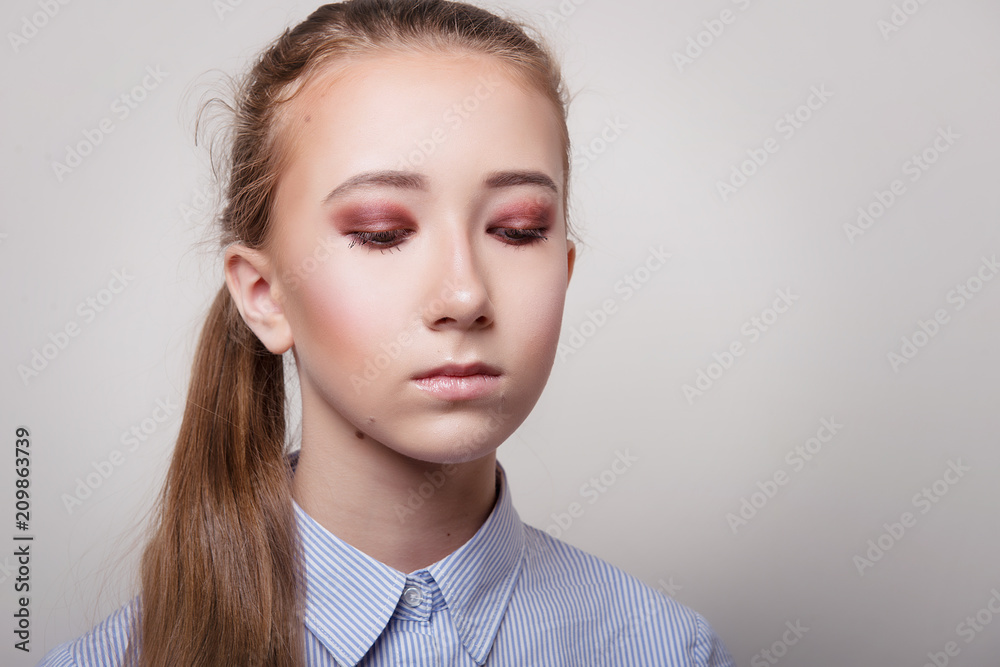 Girl in blue shirt and with bright makeup on closed eyes on gray background close-up. Girl in blue shirt and with bright makeup on closed eyes on gray background close-up.