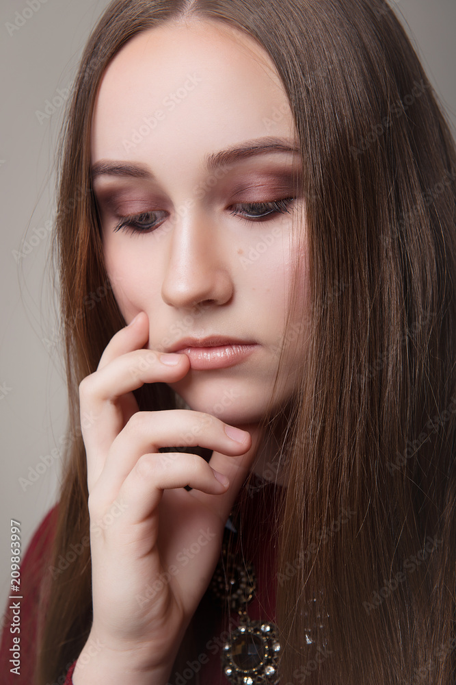 The girl is brown-haired with long flowing hair in a Burgundy dress and with makeup in closed eyes on a gray background close-up.