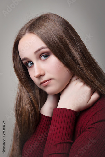 The brown-haired girl with long straight hair and makeup keeps herself around the neck on a gray background close-up.