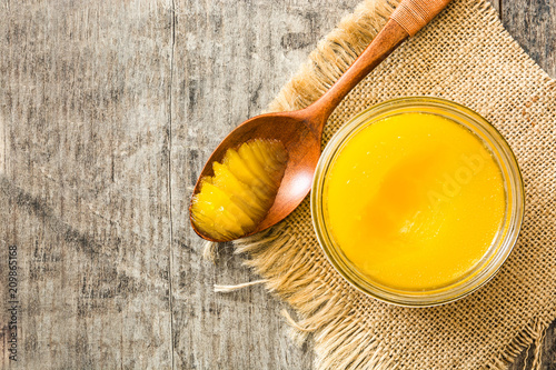 Ghee or clarified butter in jar and wooden spoon on wooden table. 