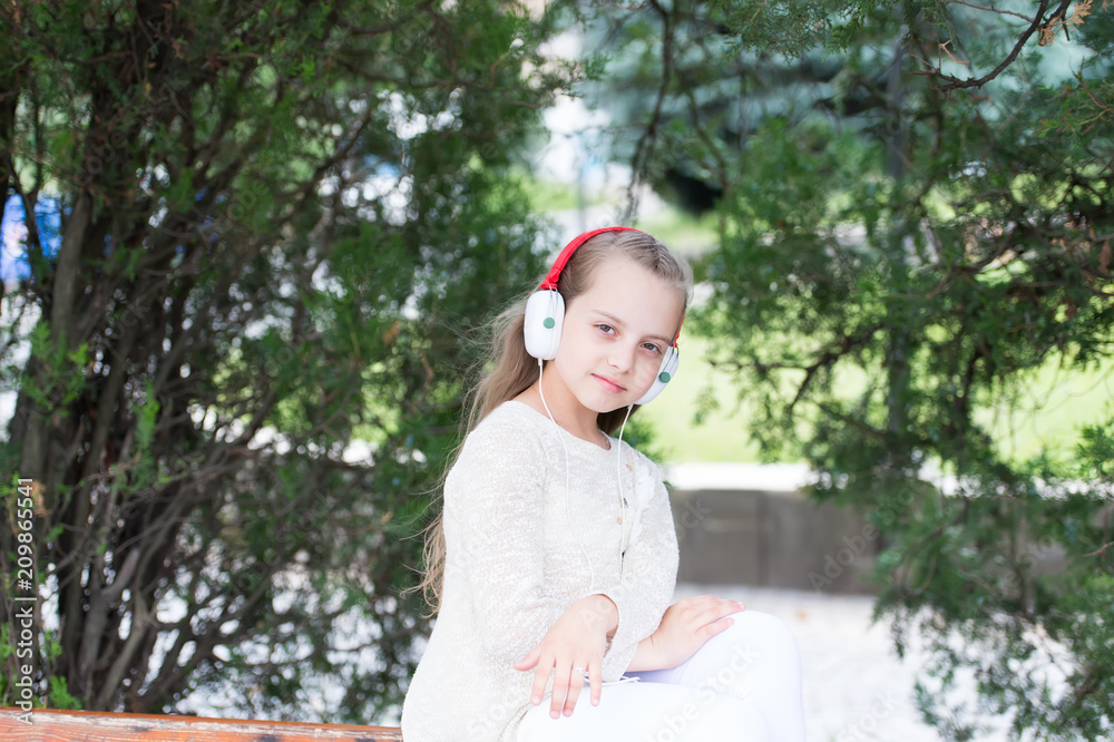 Naklejka premium Child enjoy music in headphones outdoor. Fashion kid and modern technology. Little girl listen music in summer park. Melody sound and mp3. Summer vacation rest and fun