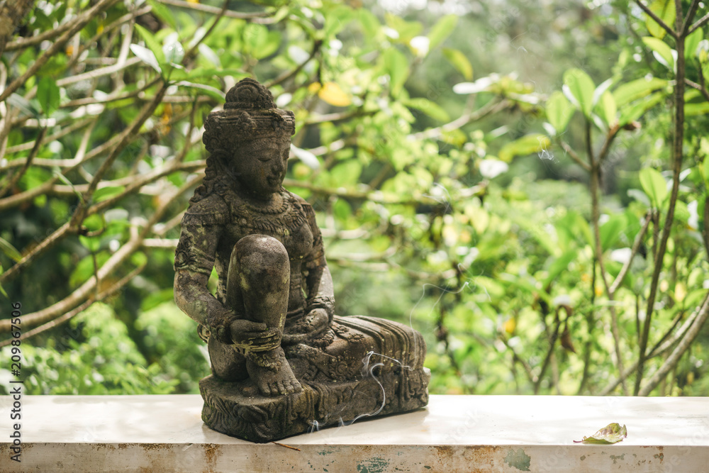 close up view of traditional statue and plants with green leaves on background, ubud, bali, indonesia close up view of traditional statue and plants with green leaves on background, ubud, bali, indonesia